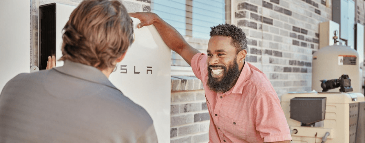 Two men talk over a Tesla Powerwall battery backup system