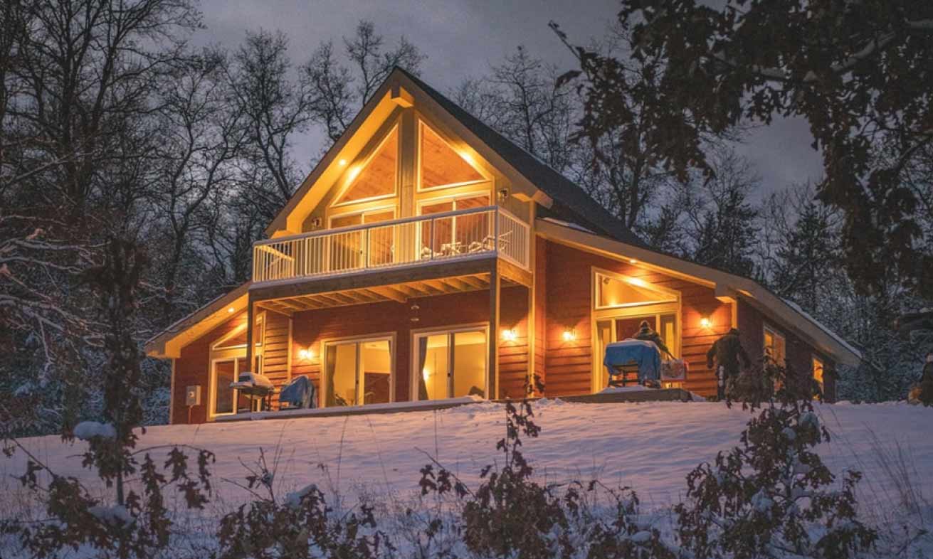 A cozy cabin nestled in the woods, featuring a porch adorned with warm lights.