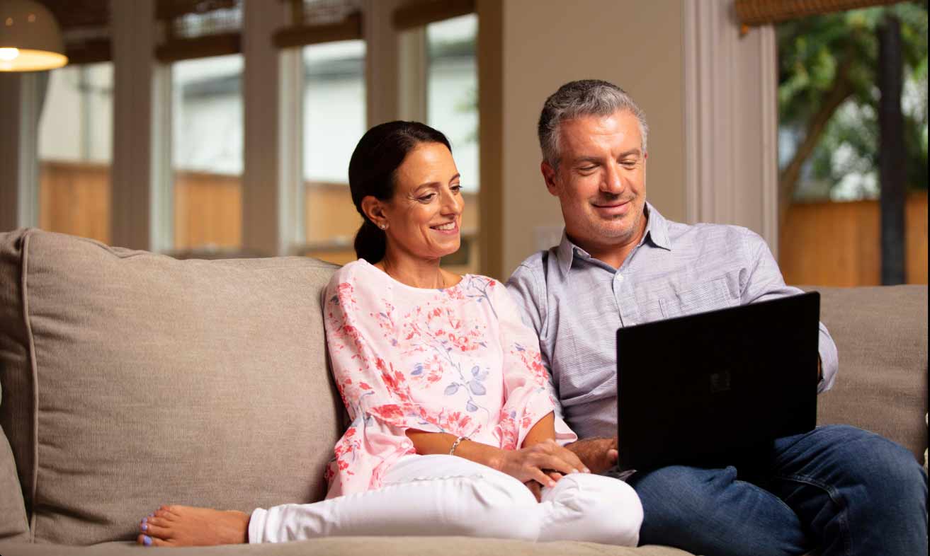 A man and woman sitting on a couch with a laptop